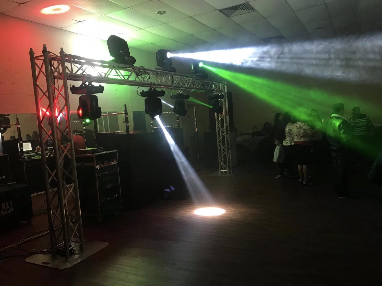 Estructura de truss con luces robóticas proyectando haces blancos y verdes sobre una pista de baile